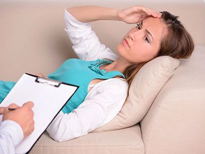 Una mujer está acostada en un sofá mientras un hombre escribe en un portapapeles.