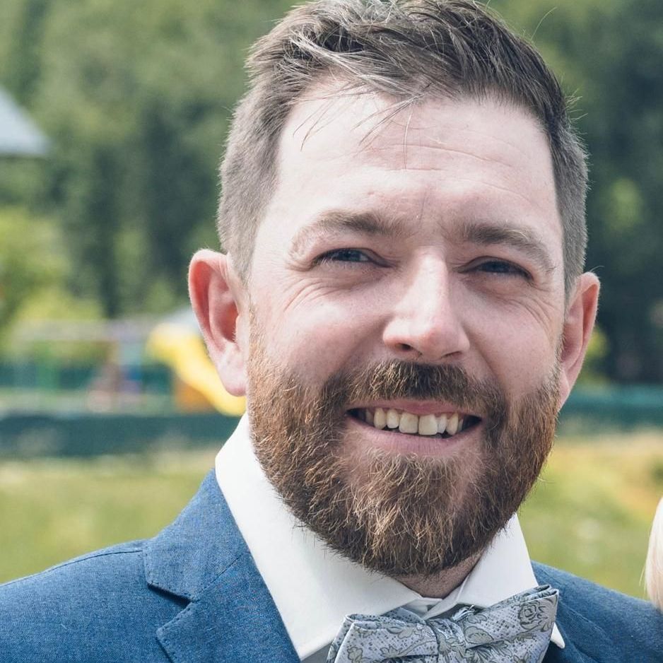 Ein Mann mit Bart, Anzug und Fliege trägt, lächelt.