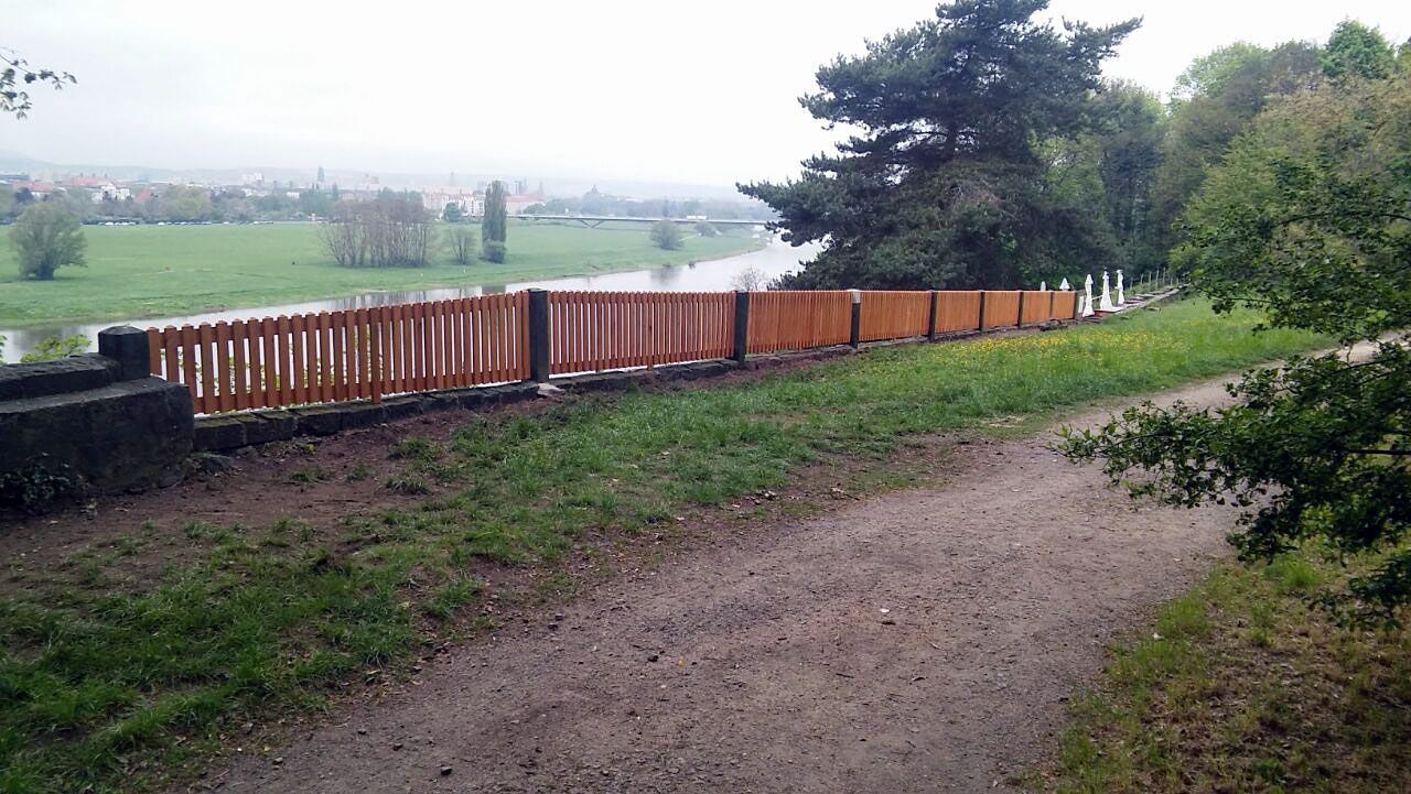 Holzzaun entlang eines Uferwegs, bewölkter Tag.