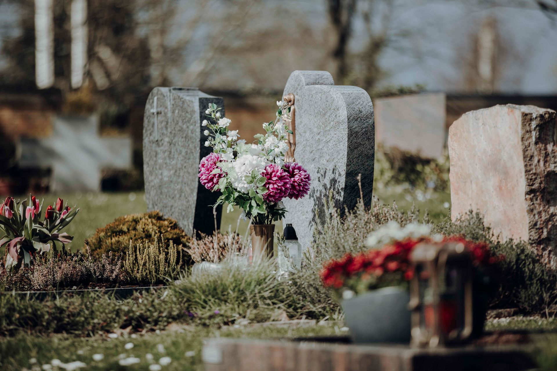 Auf dem Friedhof gibt es viele Gräber mit Blumen.
