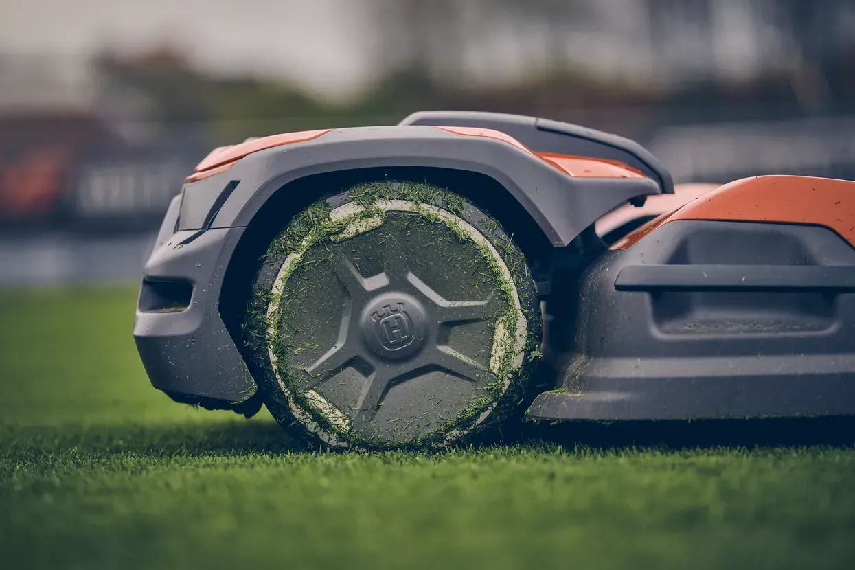 Un détail de roue de robot tondeuse pleine d'herbe.