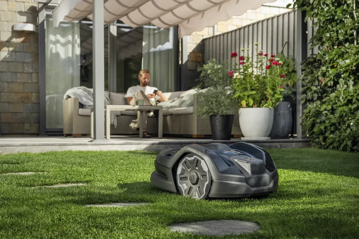 Un robot tondeuse au premier plan d'un homme assis dans sa véranda.