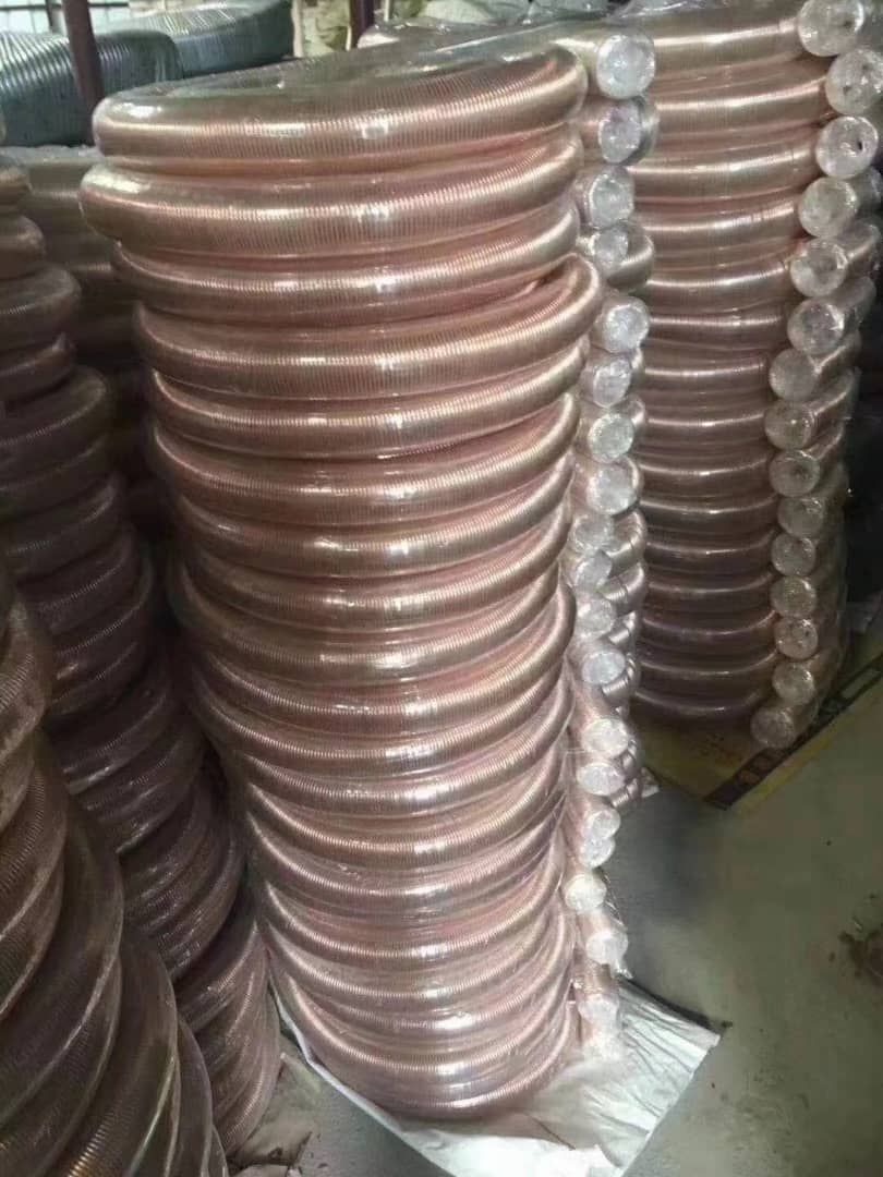 Pilas de tubos metálicos enrollados de color cobrizo, envueltos en plástico, en un almacén.