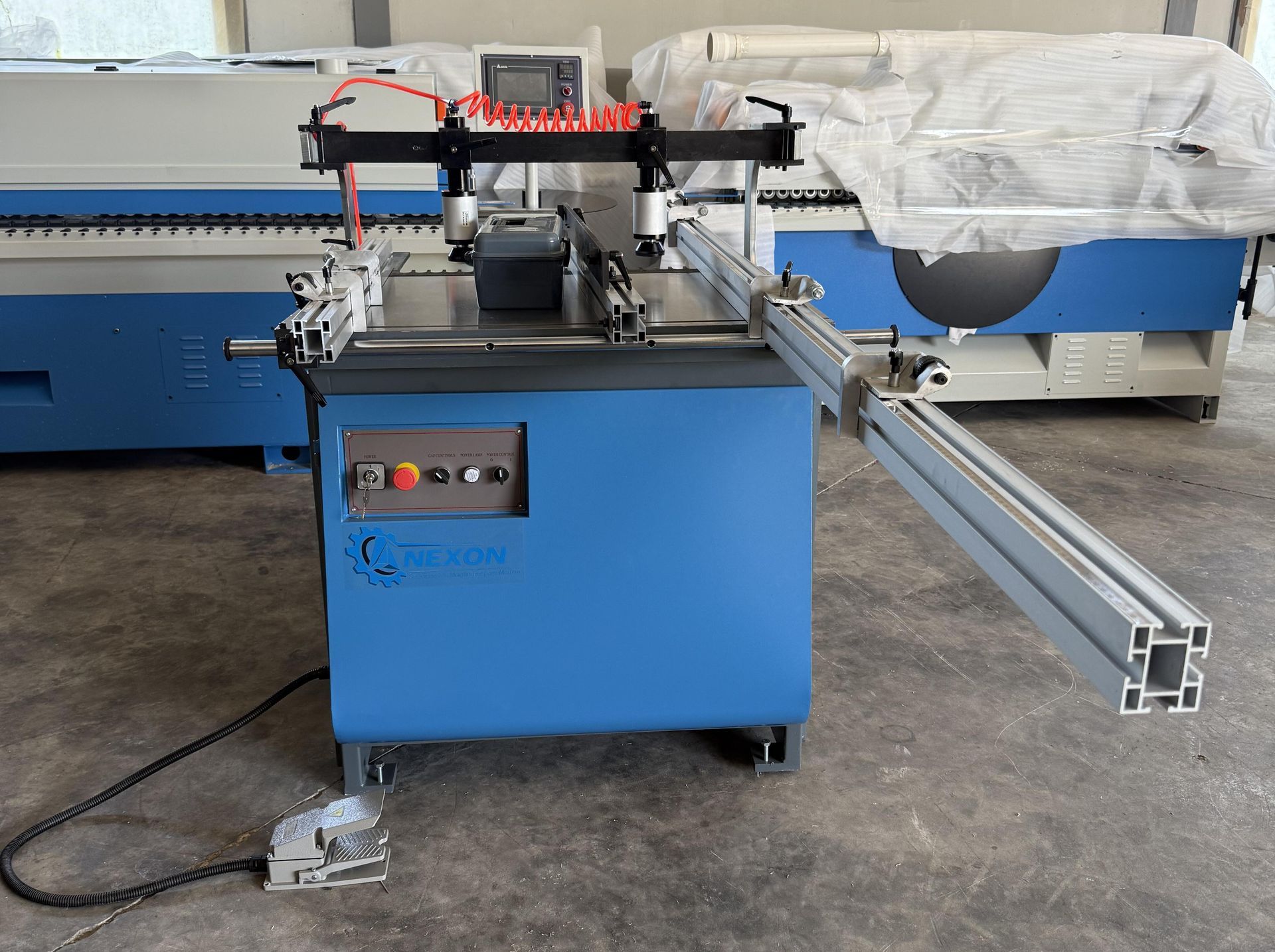 Máquina industrial azul con un largo raíl metálico en un taller, cubierta con plástico blanco