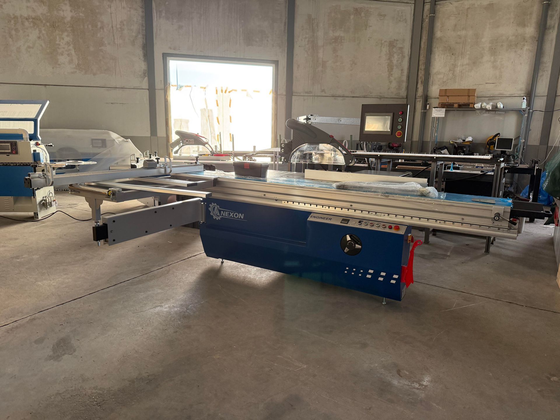 Sierra de mesa industrial con base azul y rieles plateados en un taller, rodeada de madera y herramientas