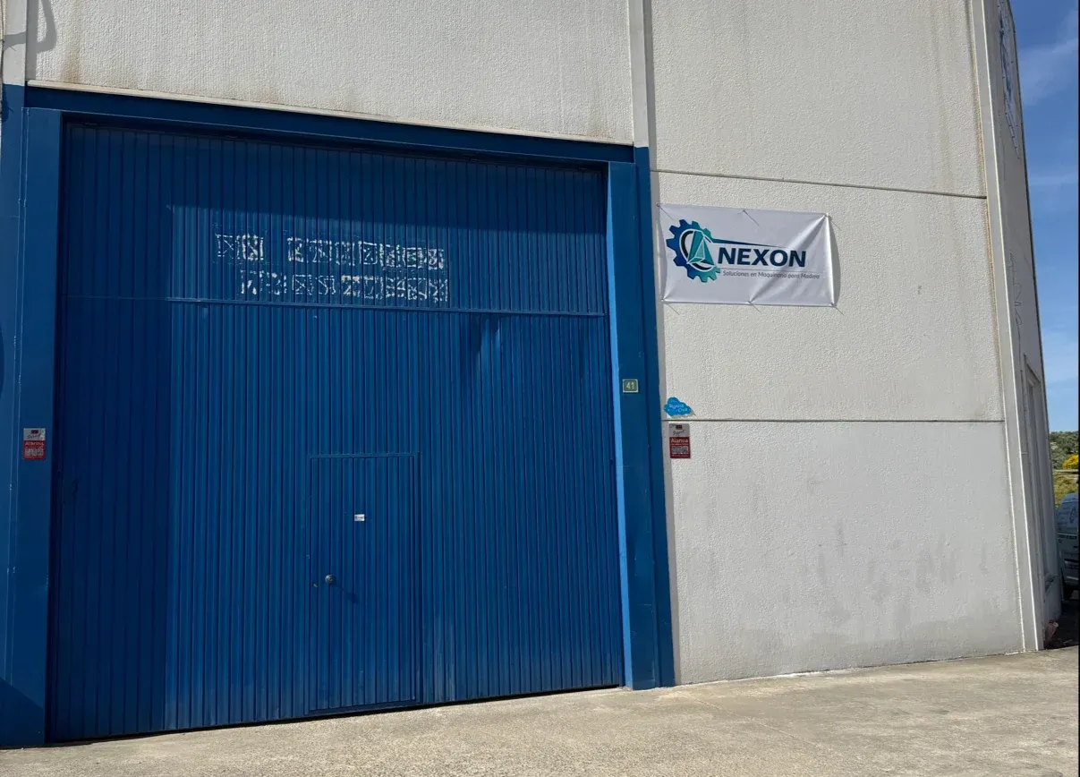 Portón industrial azul en un edificio de hormigón, con un letrero de Nexon al lado