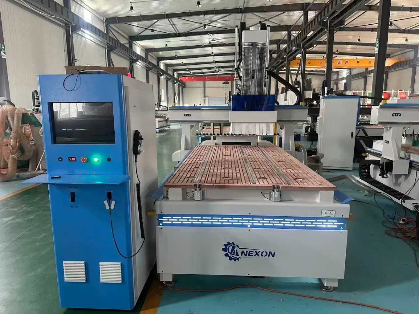 Fresadora CNC industrial azul en una fábrica, con un panel de control y una mesa de trabajo cargada de materiales rojos.
