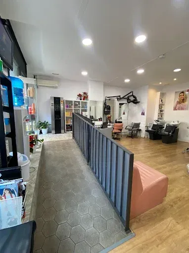 Interior de peluquería con estaciones de peinado, productos y una zona de espera con un banco rosa.