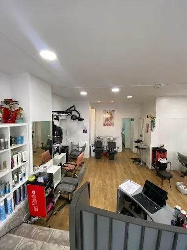 Interior de peluquería con estaciones de peinado, productos en estantes y mostrador de recepción.