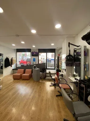 Interior de peluquería con estaciones de peinado, zona de espera y grandes ventanales.