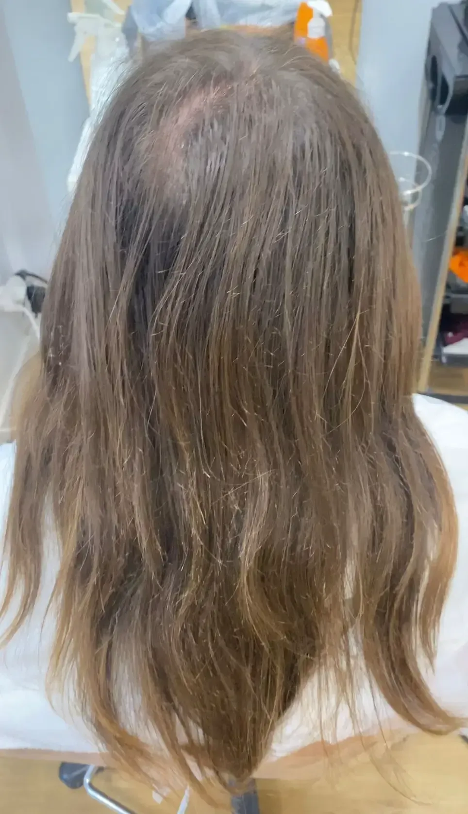 Cabello rubio rizado y extendido. La persona lleva una capa blanca, presumiblemente en una peluquería.