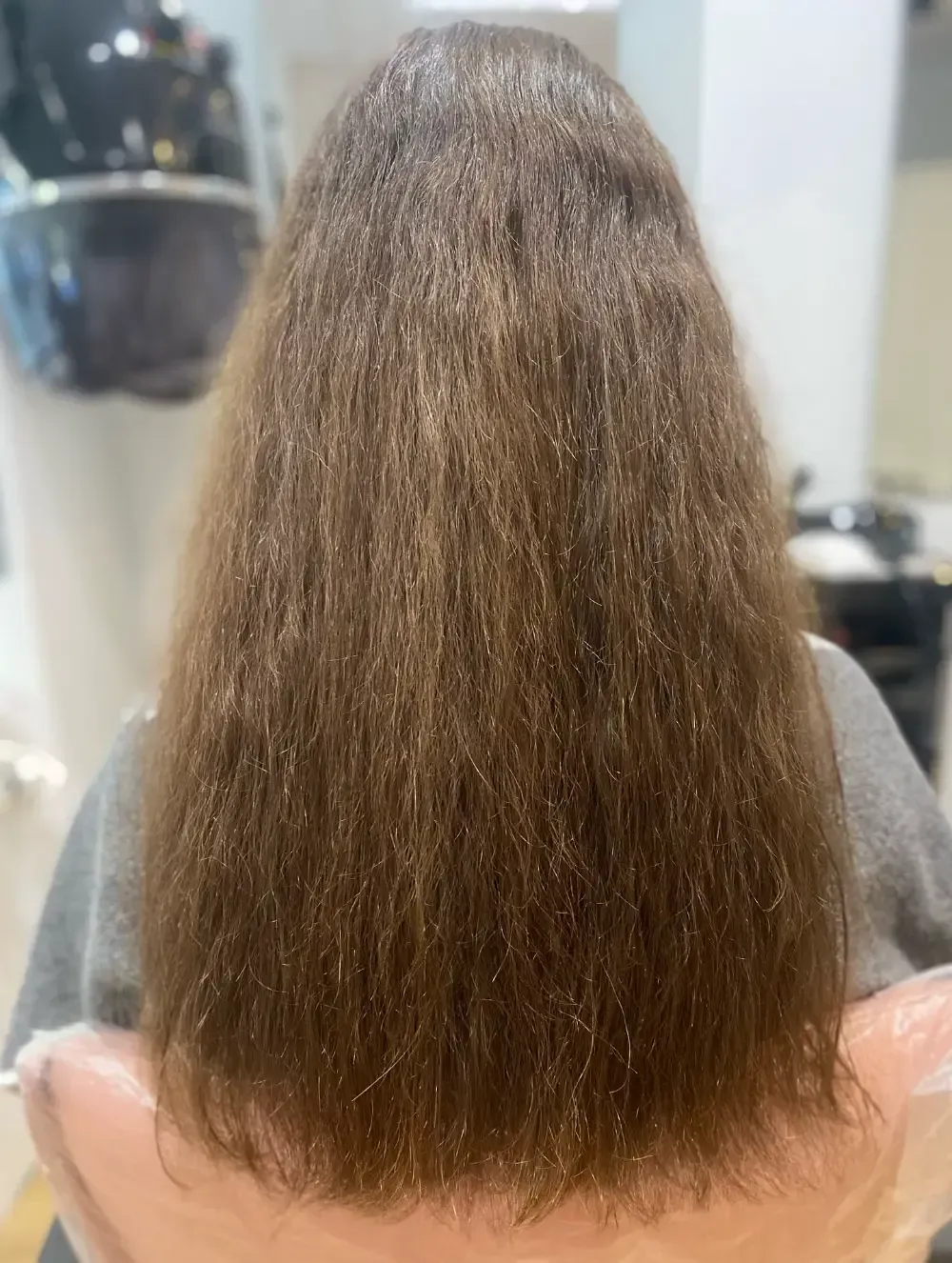 Persona en una silla de salón con cabello castaño largo y encrespado.
