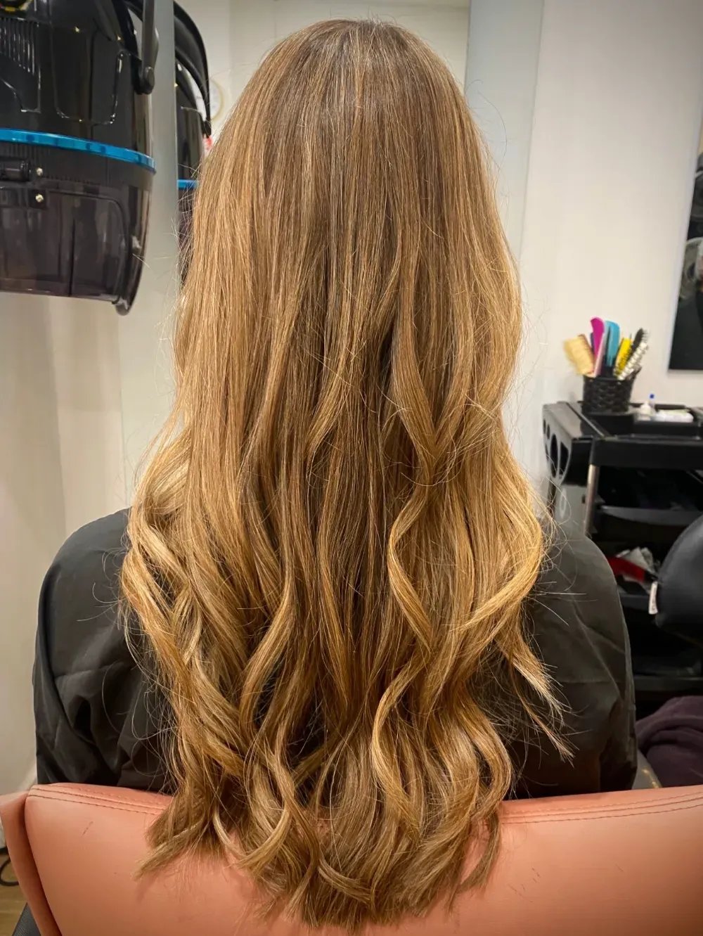 Mujer con cabello rubio ombré largo y ondulado, vista posterior.