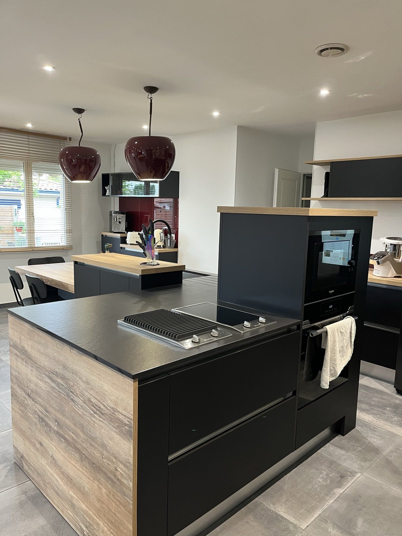 Une cuisine ouverte avec un grand îlot central en L, piano gaz et plaque à induction.