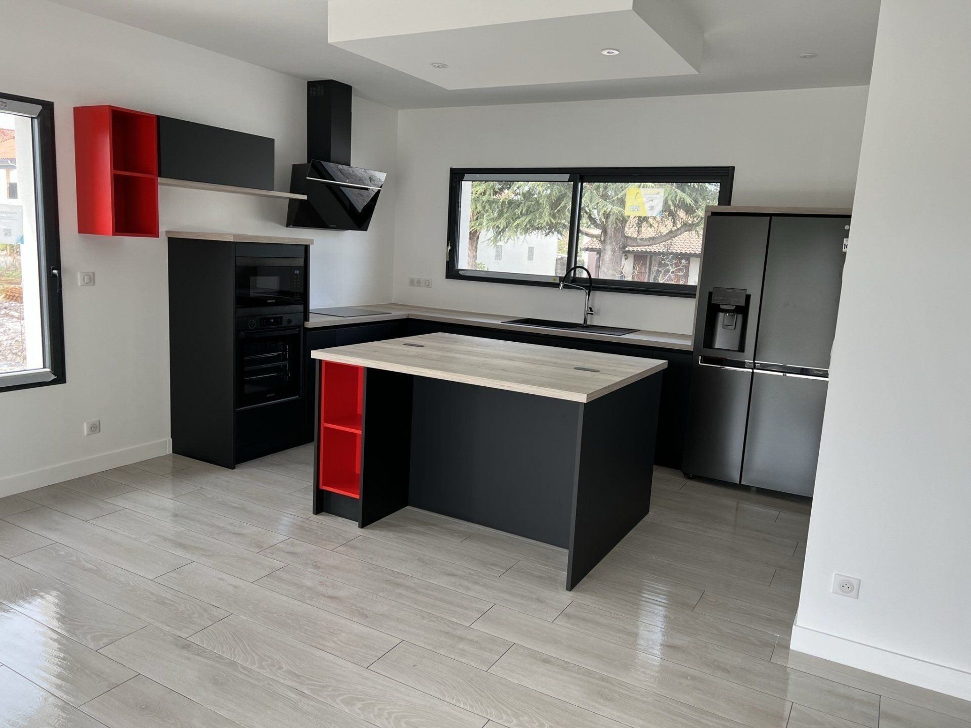 Photo d'une cuisine noire et rouge moderne dans une maison, grand frigo et îlot central.