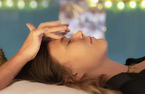 Una mujer está acostada en una cama con la mano en la frente.
