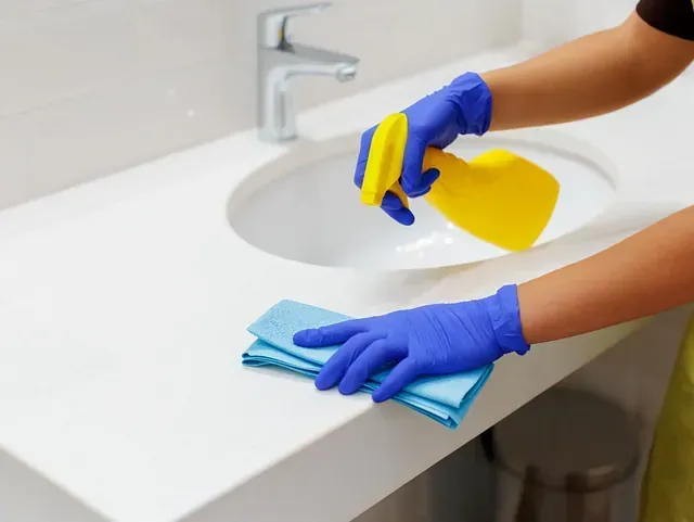 Una persona que lleva guantes azules está limpiando el lavabo del baño.