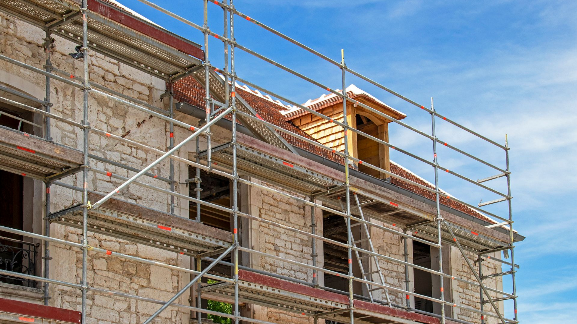 Des échafaudages entourent un bâtiment en pierre avec une lucarne.