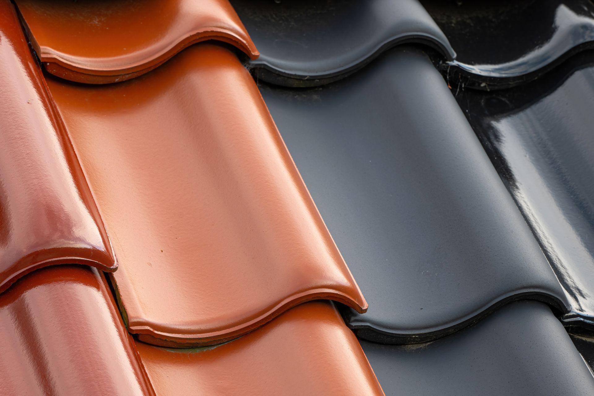Gros plan sur trois rangées de tuiles de toit en céramique brillante : brun-rouge, brun-orangé et noires.