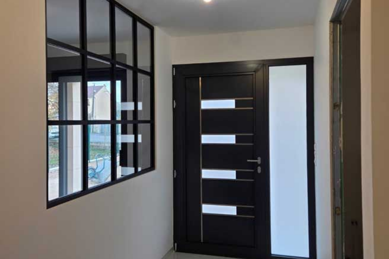 Couloir avec porte noire, imposte et croisillons de fenêtre, le tout en verre dépoli.