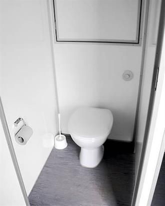 Eine weiße Toilette mit einer Toilettenbürste in einem Badezimmer.