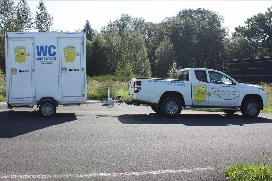 Ein weißer LKW zieht einen Anhänger mit der Aufschrift „WC“
