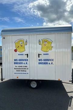 Ein weißer Anhänger mit zwei gelben Zeichentrickfiguren darauf steht auf einem Parkplatz.