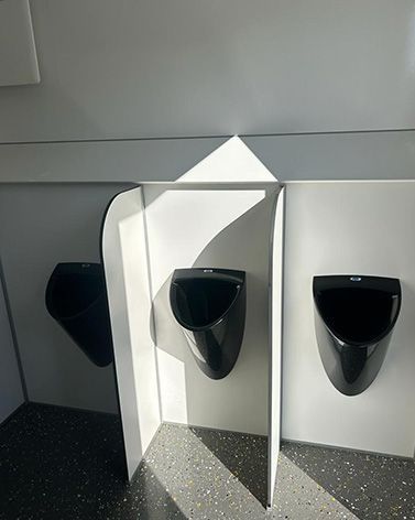 In einer öffentlichen Toilette stehen drei schwarze Urinale nebeneinander.