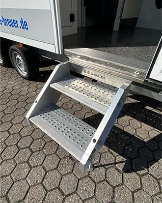 Auf einem gepflasterten Gehweg ist ein Anhänger mit daran befestigter Treppe geparkt.