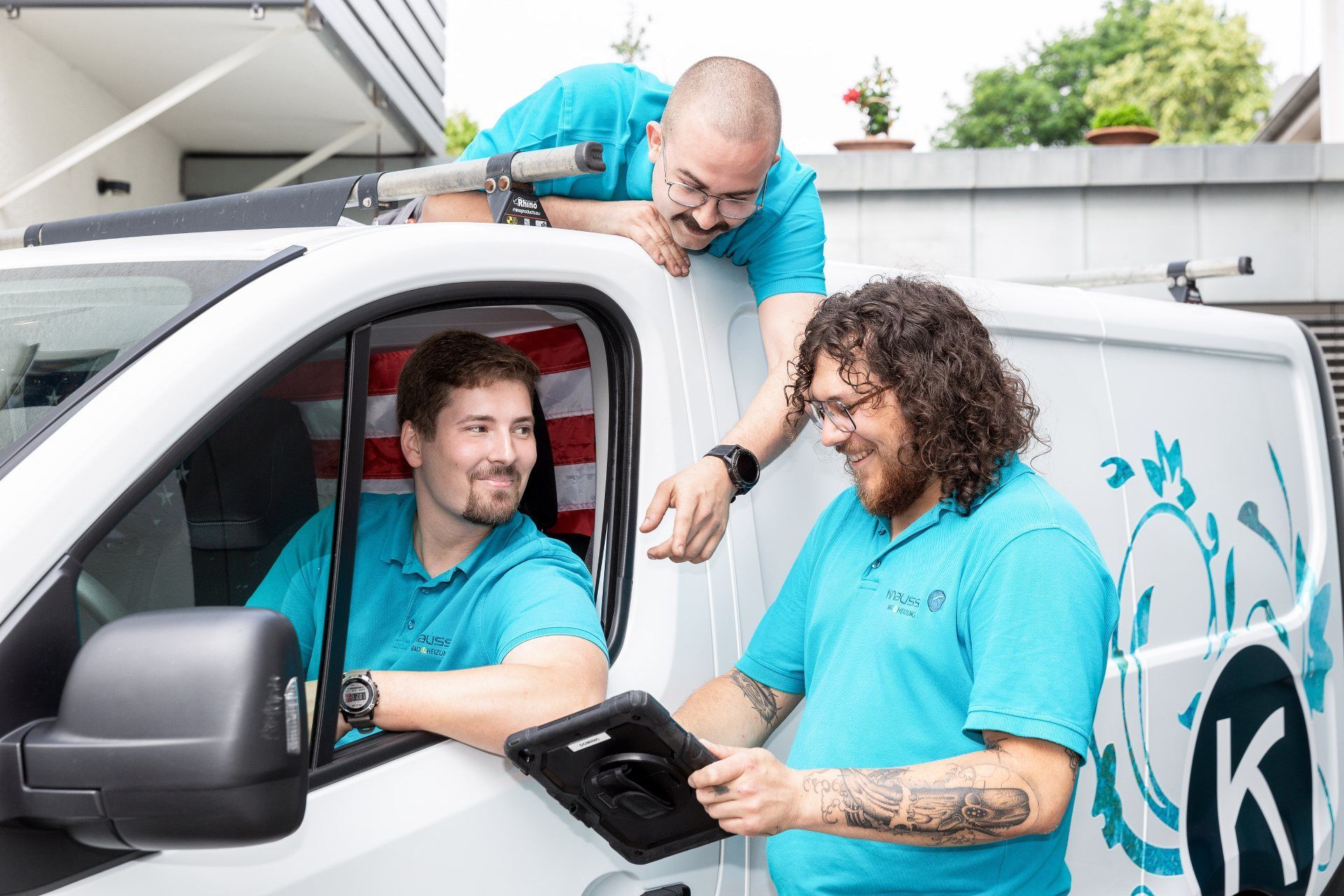 Zwei Männer stehen neben einem weißen Wagen und schauen auf ein Tablet.