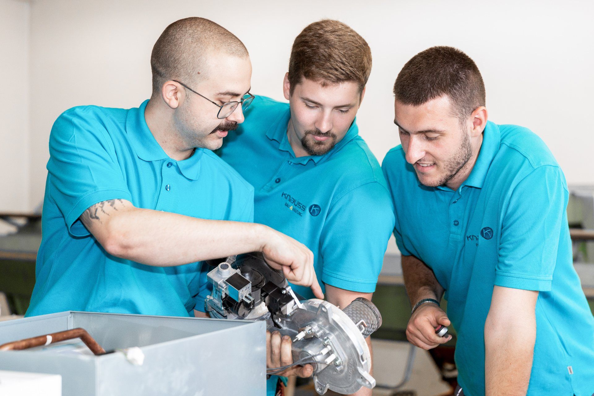 Drei Männer in blauen Hemden arbeiten an einer Maschine.