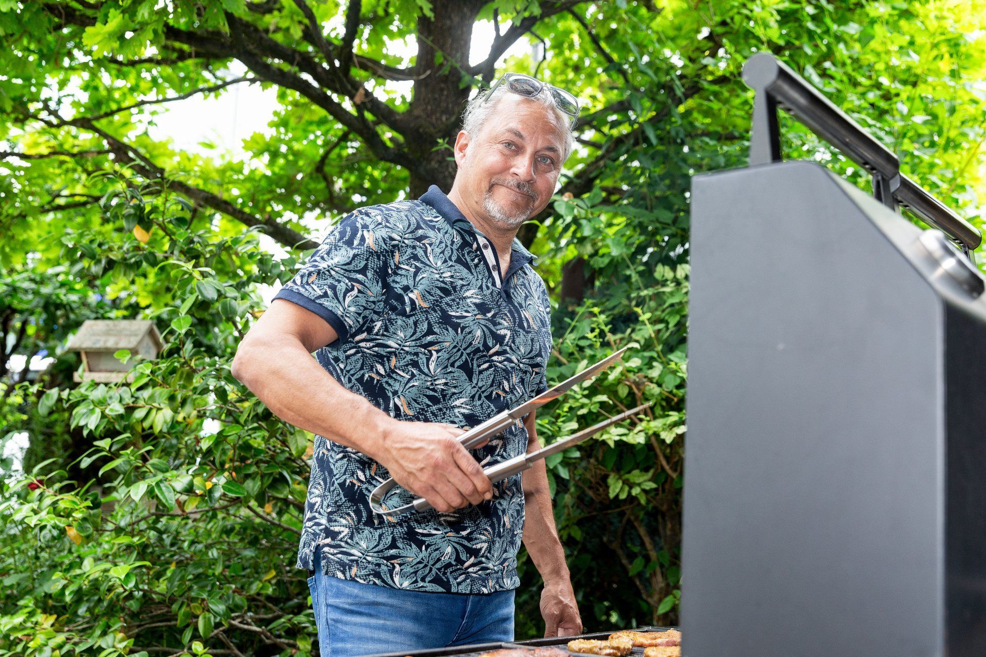 Ein Mann steht mit einer Zange vor einem Grill.