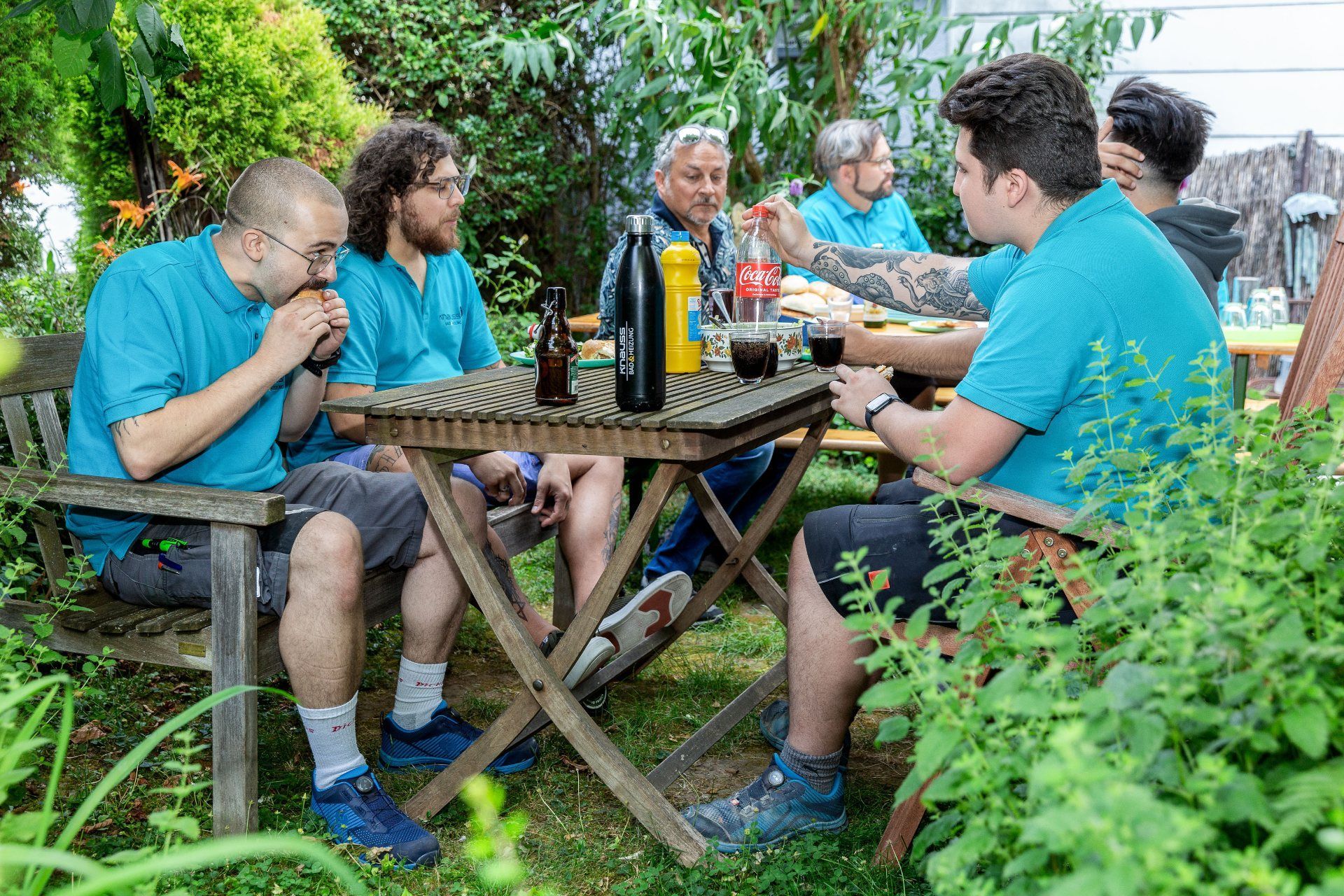 Eine Gruppe von Leuten sitzt in einem Garten um einen Tisch.