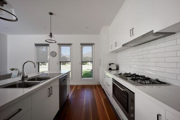Bright modern galley kitchen with white cabinets, subway tile, black appliances, and hardwood floor