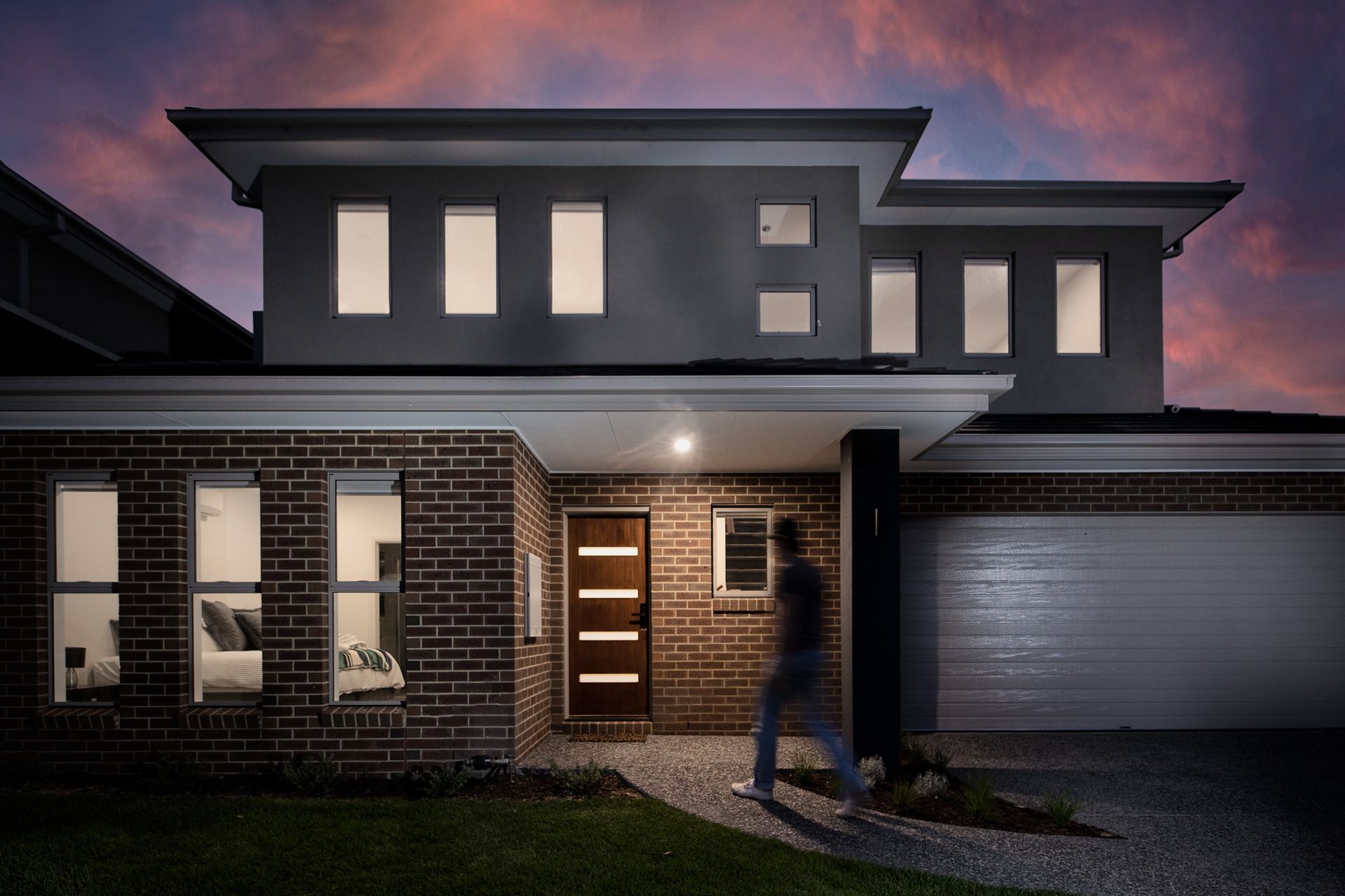 Modern two-story house at dusk with lit windows, brick facade, and garage under a purple sky
