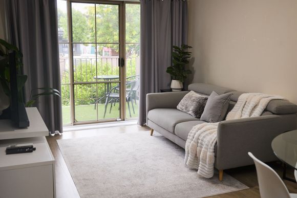 Bright living room with gray sofa, large window, white rug, and balcony view