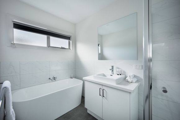 Bright white bathroom with a bathtub, vanity sink, large mirror, and frosted window.