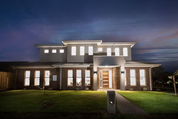 Modern two-story house lit up at dusk with a green lawn and cloudy twilight sky