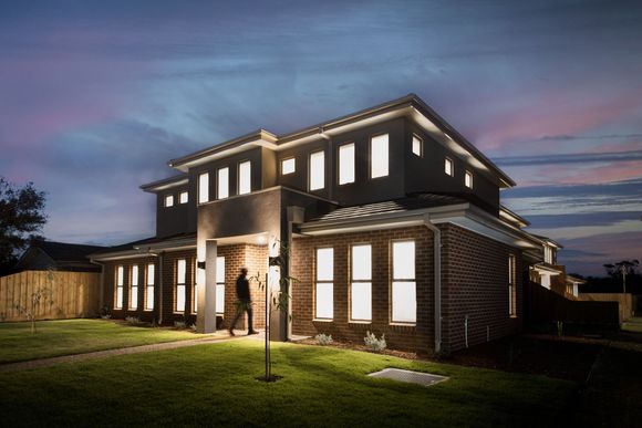 Modern brick house at dusk with warm lit windows and a manicured lawn under a colorful twilight sky