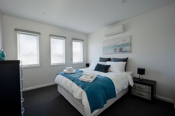 Bright bedroom with a bed, teal bedding, three windows, and white walls