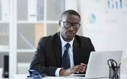 A man in a suit and tie is sitting at a desk using a laptop computer.