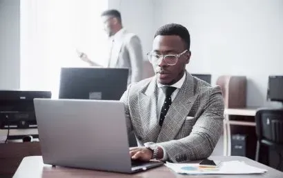 A man in a suit and tie is sitting at a desk using a laptop computer.