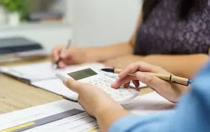 A person is using a calculator while another person is writing on a clipboard.