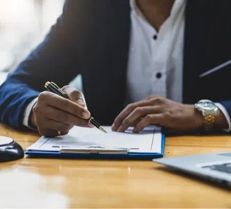 A man is sitting at a table writing on a clipboard with a pen.
