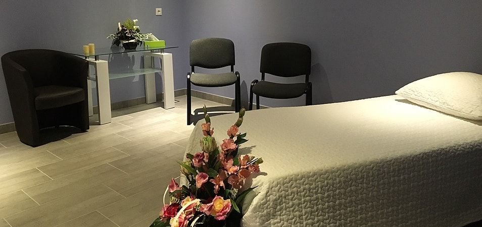 Vue d'un lit avec une gerbe de fleurs au pied et de deux chaises à l'arrière-plan