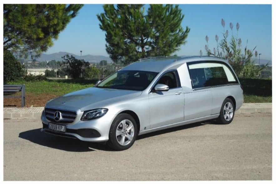 Un coche fúnebre Mercedes Benz plateado está estacionado al costado de la carretera.