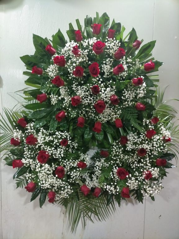 Una corona con rosas rojas y flores blancas de aliento de bebé.