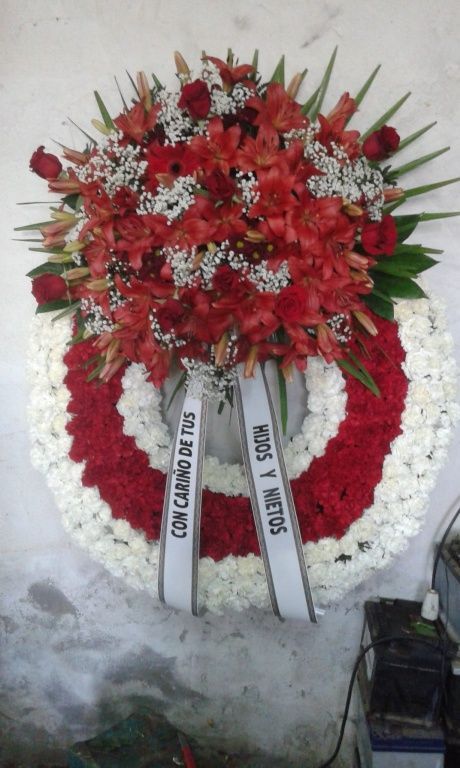 Una corona de flores rojas y blancas con una cinta que dice con camino de tus