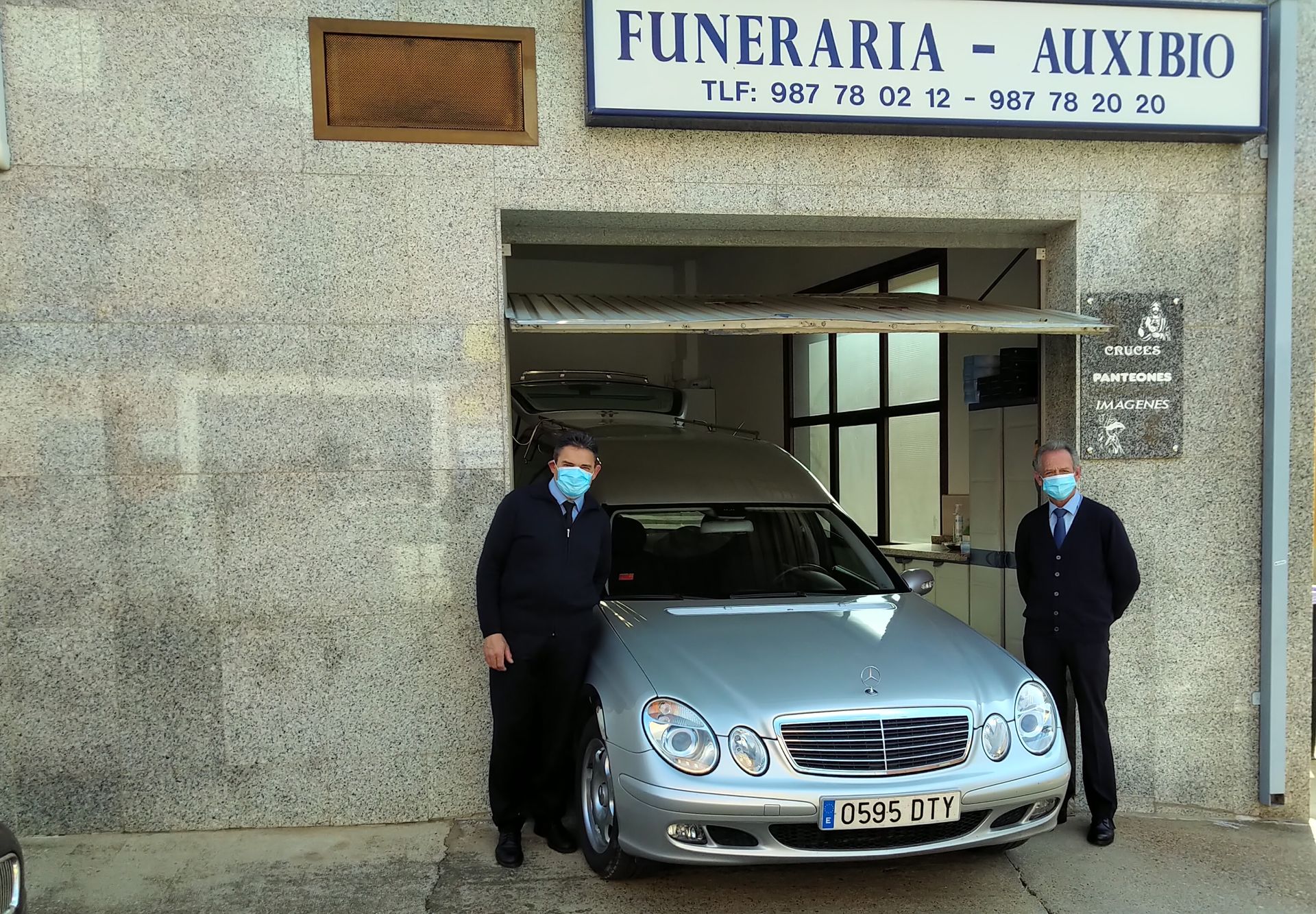Dos hombres con mascarillas se encuentran frente a un automóvil plateado.