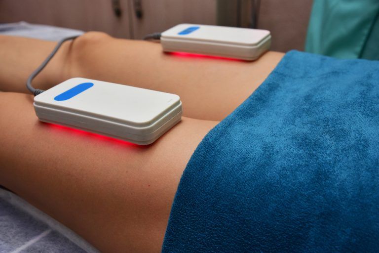 Des mains massent le dos d'une personne allongée sur une serviette rose, en lui appliquant une lotion.